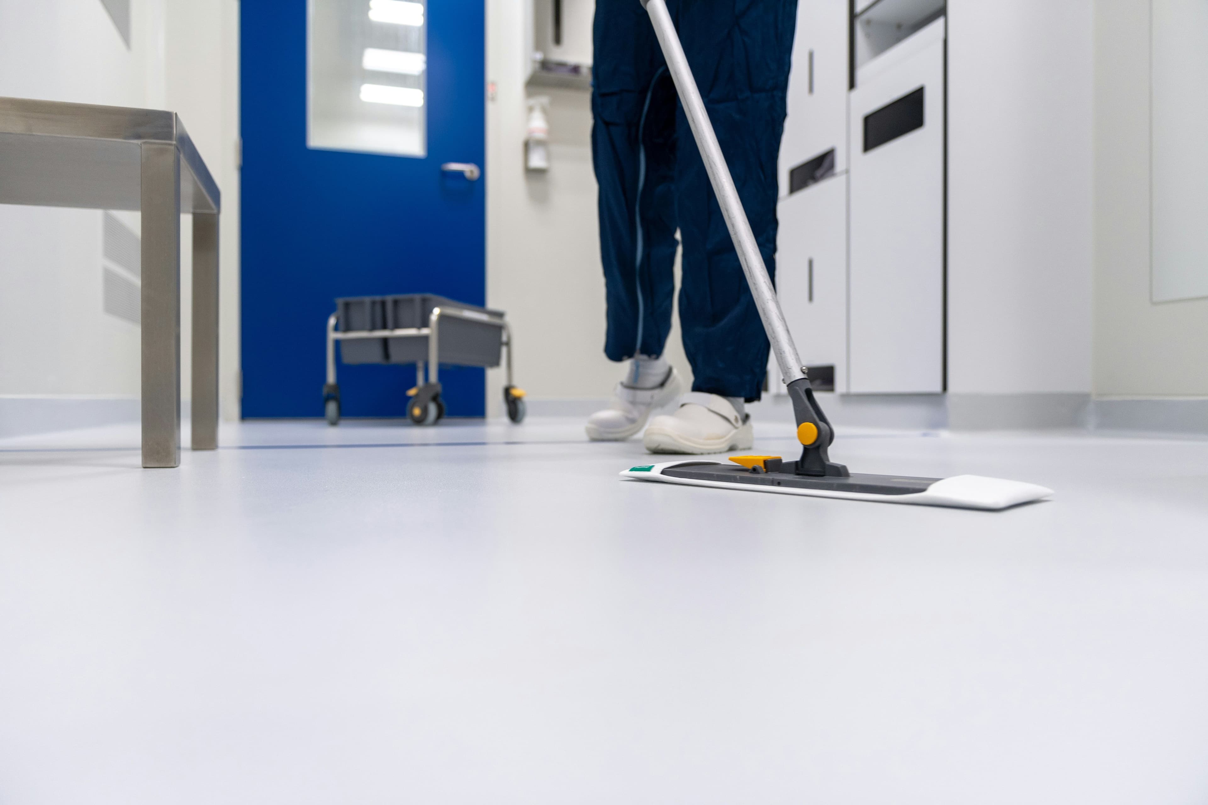 Person mopping a pristine, light-colored floor in a sterile cleanroom environment.